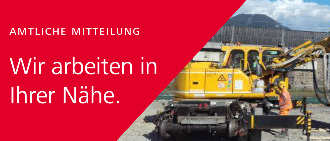 Ein Bauarbeiter in einer orangefarbenen Weste und einem gelben Helm bedient einen gelben Kran mit verschiedenen Schildern auf einer Baustelle.