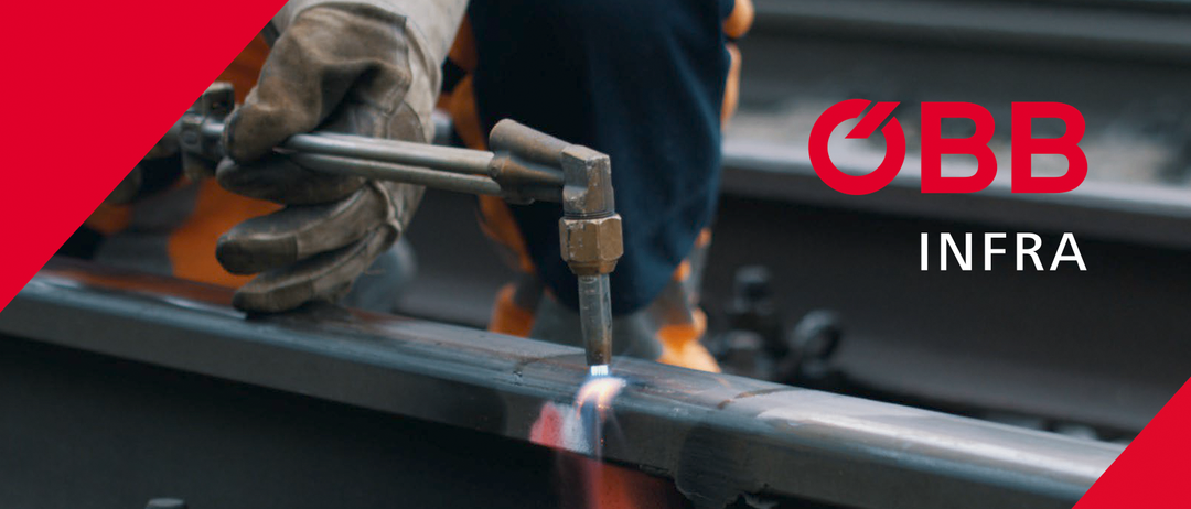Eine Hand in einem Arbeitshandschuh hält ein Metallwerkzeug, möglicherweise ein Schraubenschlüssel, vor einem roten Hintergrund.