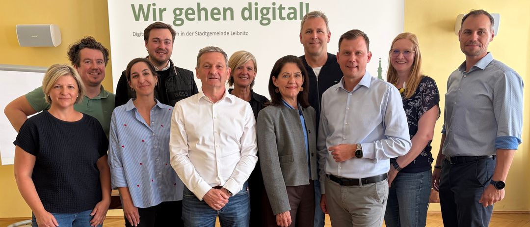 Eine Gruppe von Menschen steht vor einem Schild mit der Aufschrift 'Wir gehen digital'. Sie posieren für ein Foto.