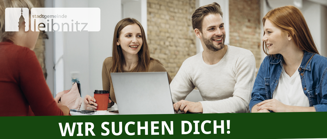 Ein lächelnder Mann und eine Frau sitzen zusammen an einem Schreibtisch, mit einem Laptop und einer Kaffeetasse vor ihnen, lächeln und schauen in die Kamera.