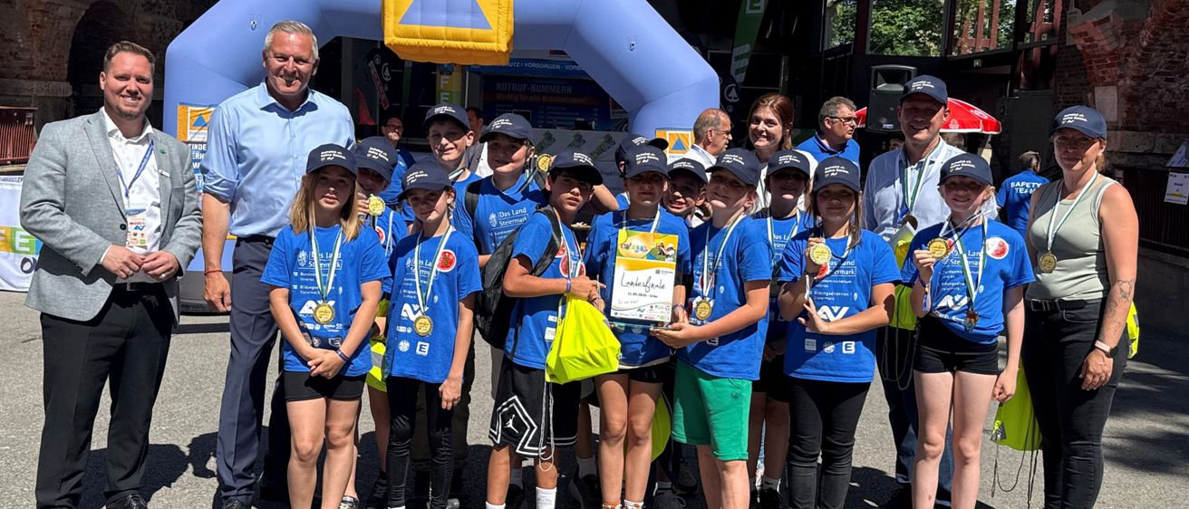 Eine Gruppe von Kindern und Erwachsenen in blauen Shirts posiert für ein Foto vor einem Bogen. Sie tragen alle Medaillen und einige halten Urkunden.