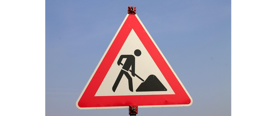 Ein dreieckiges Straßenschild mit einem Mann, der Erde schaufelt, was auf bevorstehende Straßenarbeiten hinweist.