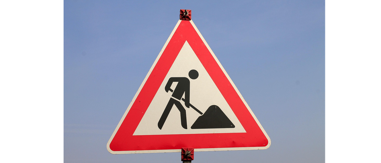 Ein dreieckiges Straßenschild mit einem Mann, der Erde schaufelt, was auf bevorstehende Straßenarbeiten hinweist.