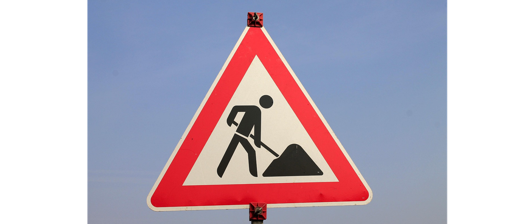Ein dreieckiges Straßenschild mit einer Person, die Erde schaufelt, was auf bevorstehende Straßenarbeiten hinweist.