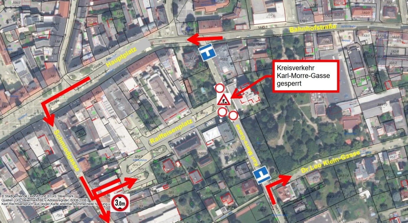 Eine Karte zeigt einen kreisförmigen Bereich mit einer 30 km/h Geschwindigkeitsbegrenzung. Beschriftungen umfassen 'Hauptplatz', 'Raiffeisenplatz', 'Karl-Morre-Gasse' und 'gesperrt'. Rote Pfeile zeigen auf bestimmte Bereiche.