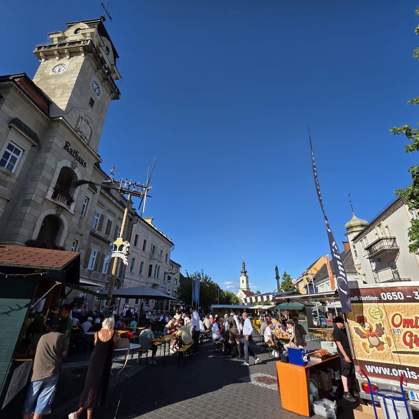 Ein geschäftiger Freiluftmarkt vor einem historischen Gebäude mit Uhrenturm, unter blauem Himmel.