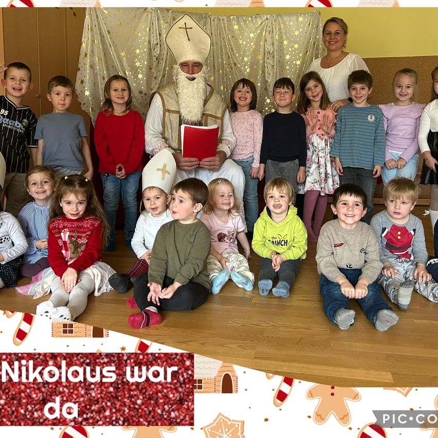 Eine Gruppe von Kindern und zwei Erwachsenen posiert für ein Foto. Der Mann in der Mitte ist als Weihnachtsmann gekleidet und hält ein Buch. Die Kinder tragen Winterkleidung. Der Hintergrund hat ein Weihnachtsthema.