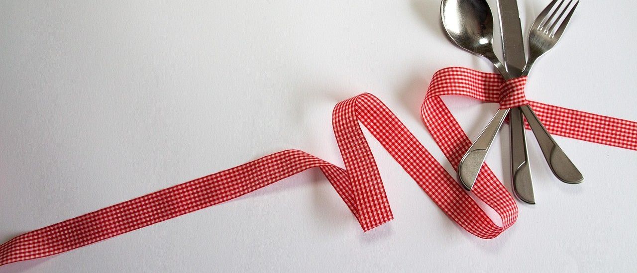 Ein rotes Band, das um eine Gabel und ein Messer geschlungen ist, auf einer weißen Oberfläche platziert.