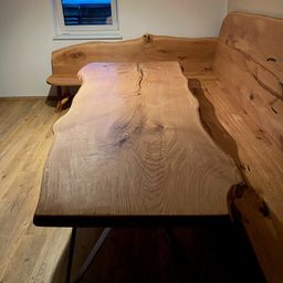 Ein hölzerner Tisch mit natürlicher Oberfläche und einer Bank dahinter. Der Tisch hat eine große Risse in der Mitte.