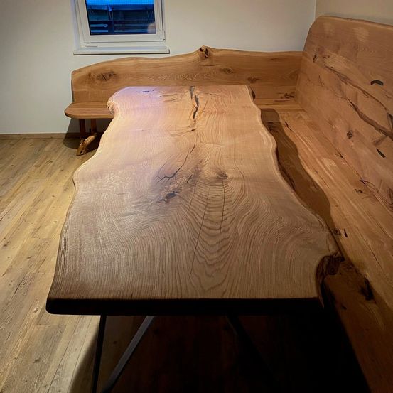 Ein hölzerner Tisch mit natürlicher Oberfläche und einer Bank dahinter. Der Tisch hat eine große Risse in der Mitte.