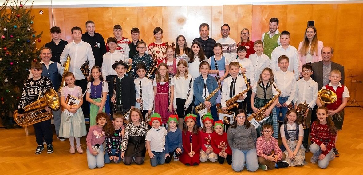 Gruppenfoto einer Schulband, bei der Schüler Musikinstrumente halten und für die Kamera in einem Raum mit einer Holzwand lächeln.