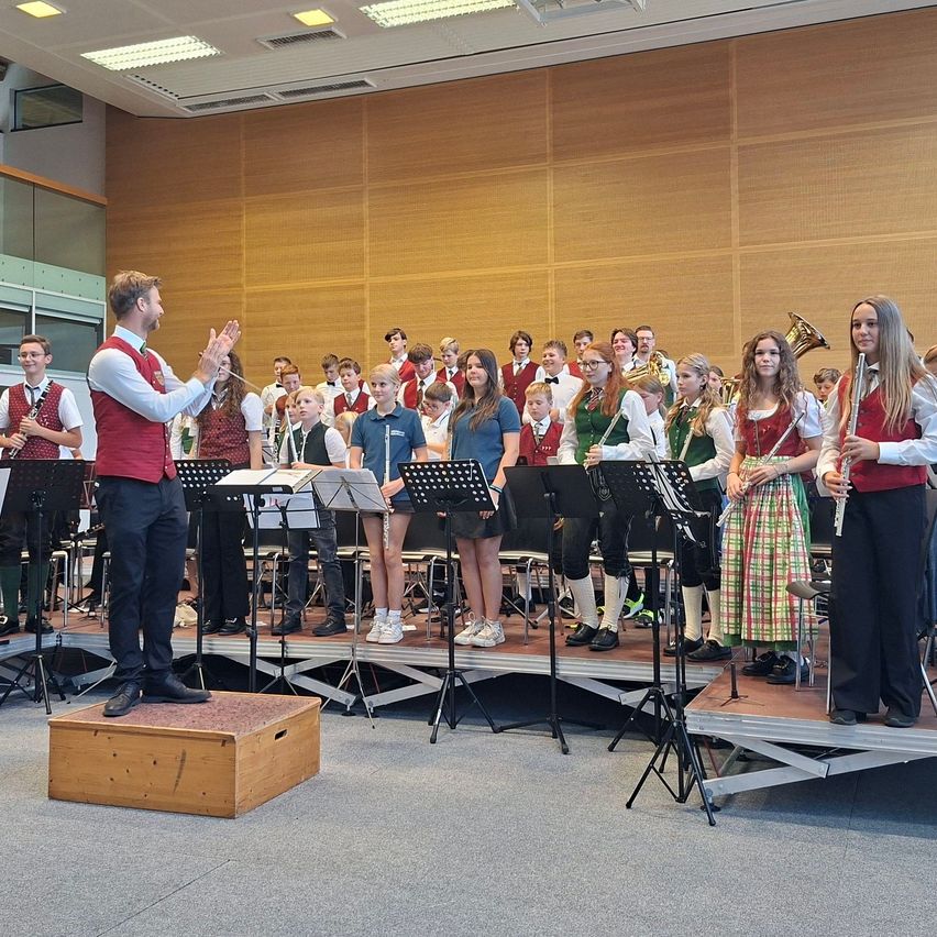 A school band is performing on stage with a conductor leading, while the audience watches.
