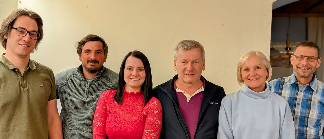 Eine Gruppe von fünf Personen, die lächelnd vor einer hellen Wand steht.