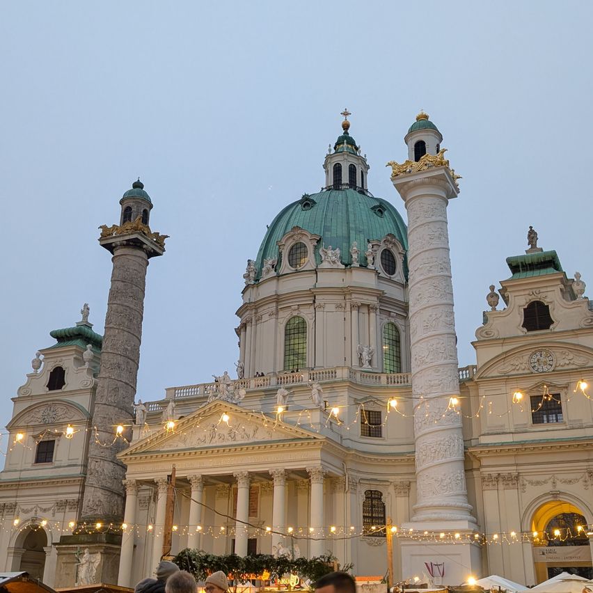 Ein großes klassisches Gebäude mit einer grünen Kuppel und aufwendigen Verzierungen. Es ist nachts mit festlichen Lichtern beleuchtet.