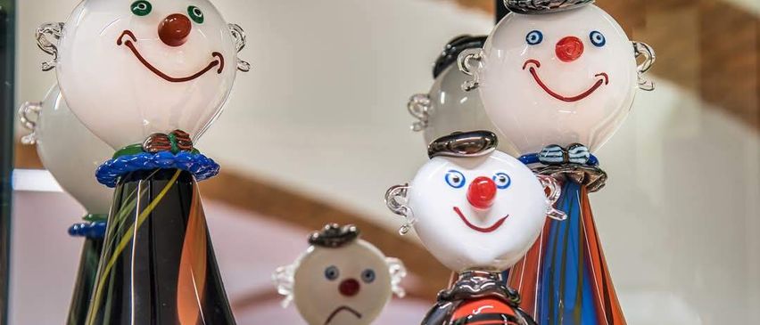 Eine Gruppe bunter Glasfiguren von Clowns, die in einem Geschäft ausgestellt sind. Jede Figur hat eine einzigartige Gesichtsausdruck und Kleidung.