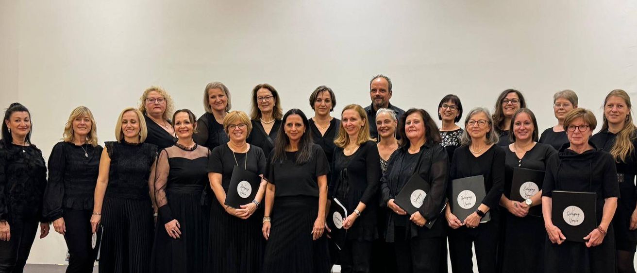 Ein Chor in Schwarz, posiert für ein Foto auf der Bühne mit Notenblättern und Lautsprechern.