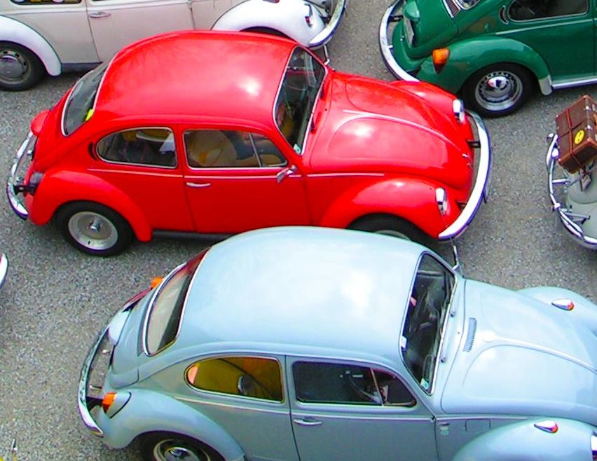 Ein Parkplatz voller klassischer Autos. Die Autos sind in verschiedenen Farben und in Reihen geparkt. Einige der Autos haben Gepäck auf dem Dach. Eine Person steht in der Nähe eines roten Autos.