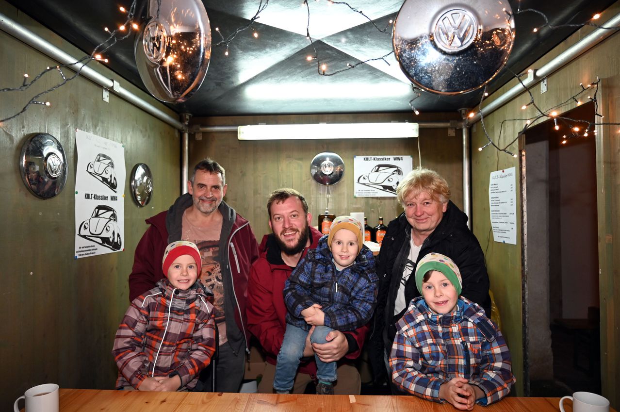 Eine Familie aus vier Erwachsenen und drei Kindern steht in einem Raum mit Volkswagen-Themendekoration. Die Erwachsenen lächeln für die Kamera.