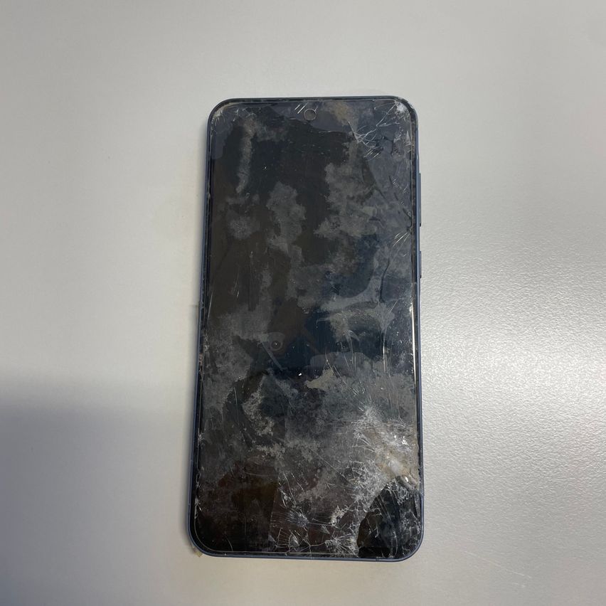 Die Rückseite eines beschädigten Smartphones mit zersplittertem Bildschirm, auf einer weißen Oberfläche platziert.