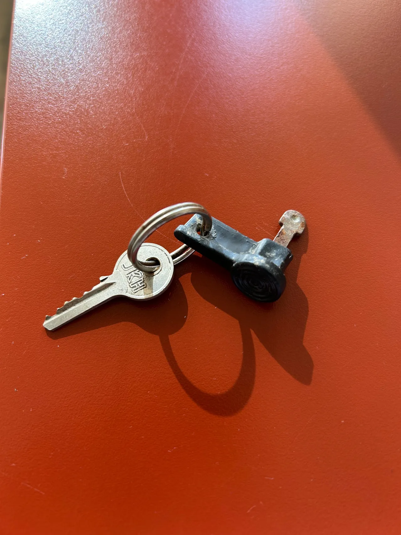 Ein silberner Schlüssel mit Schlüsselring und schwarzem Verriegelungsmechanismus auf einer roten Oberfläche.