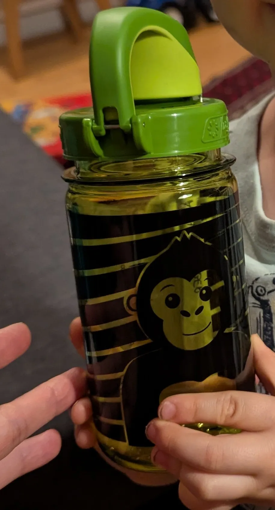 Ein Nahaufnahme einer Kinder-Wasserflasche mit einem lächelnden Affen mit goldenen Akzenten auf einem schwarz-golden gestreiften Hintergrund.