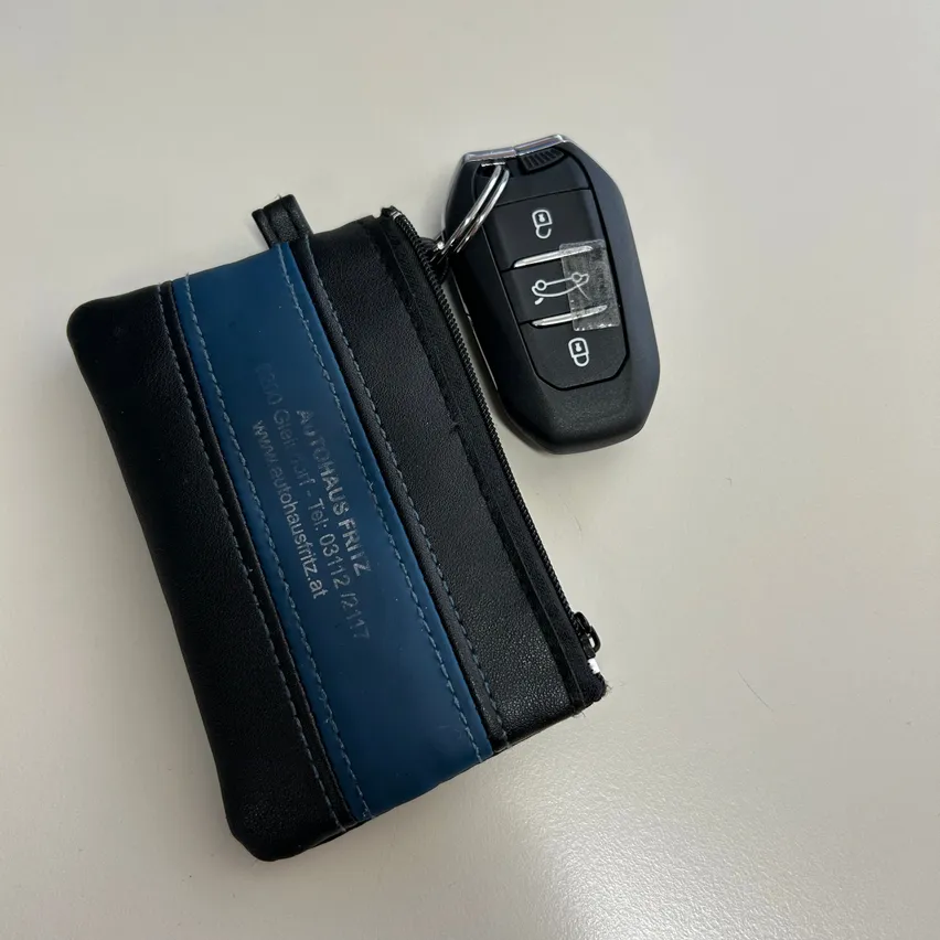 Ein schwarz-blauer Lederschlüsselanhänger mit einem Schlüssel, der auf einer weißen Oberfläche platziert ist.