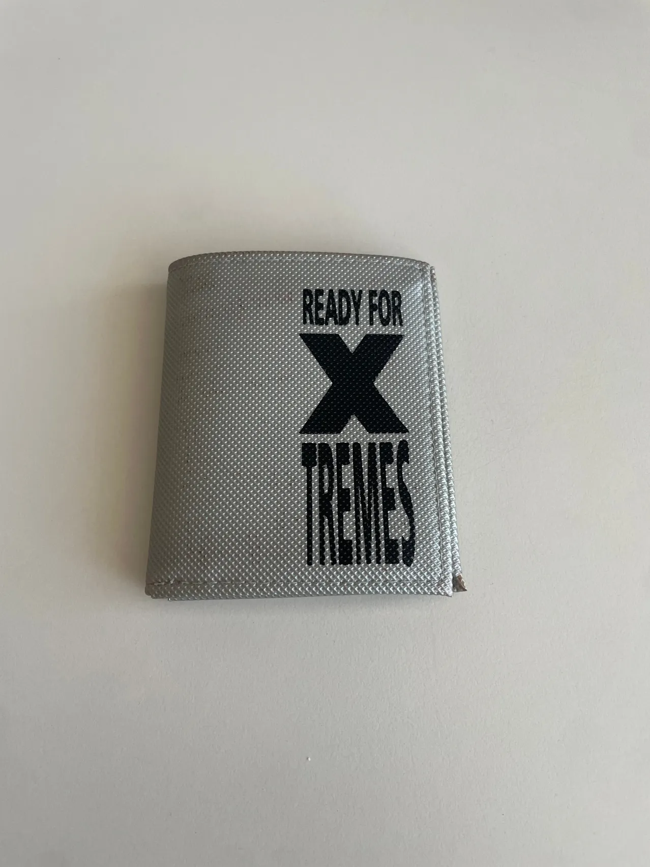 Ein Portemonnaie mit grauer Abdeckung und schwarzem Text, der 'BEREIT FÜR X TREMES' lautet.