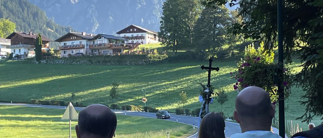 Geistliche gehen auf einer Straße mit einem Grasfeld und Bergen im Hintergrund.