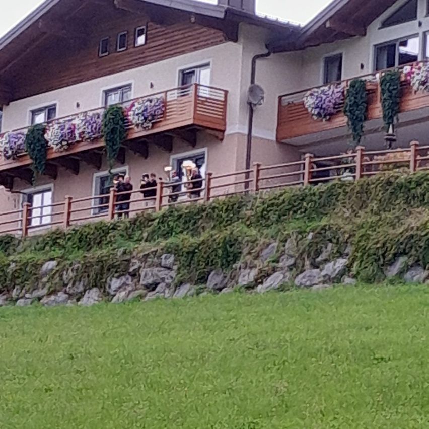 Ein Haus mit Balkonen, die mit Blumen geschmückt sind, und Menschen, die an einem sonnigen Tag draußen stehen.