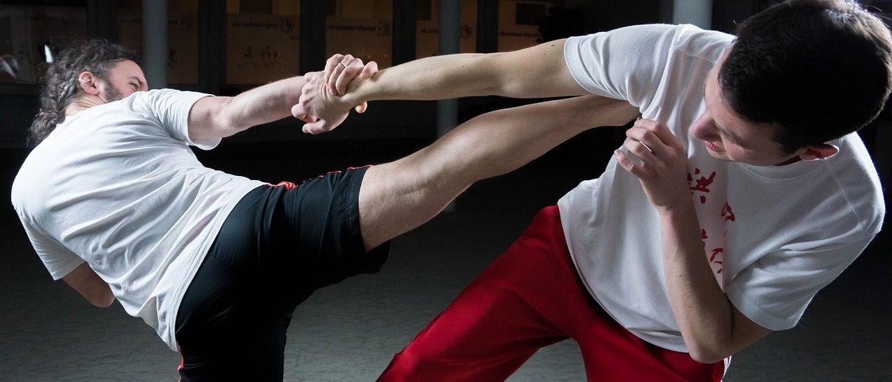 Zwei Personen in Kampfsportkleidung, eine in Weiß und die andere in Rot, sind in einem Sparring-Match engagiert.