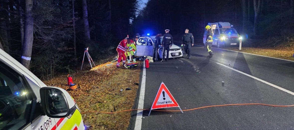 Ein Unfall auf einer Straße in der Nacht, Rettungskräfte sind am Unfallort. Feuerwehrleute und Polizisten sind anwesend.
