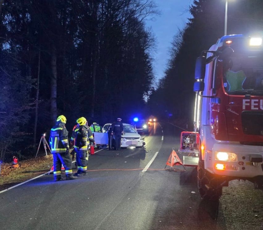 Rettungskräfte bei einem nächtlichen Unfall auf einer Landstraße. Ein Auto ist beschädigt auf der Seite, Feuerwehrleute und Polizeibeamte sind anwesend.