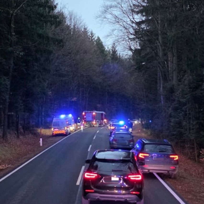 Rettungsfahrzeuge mit blinkenden Lichtern sind am Straßenrand geparkt. Mehrere Autos sind angehalten und stehen wahrscheinlich in einer Reihe, möglicherweise aufgrund eines Vorfalls.