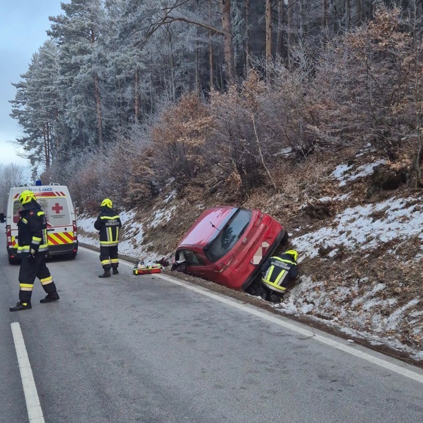 Rettungskräfte helfen bei einem von der Straße abgekommenen Auto. Ein rotes Auto liegt auf der Seite am Straßenrand.