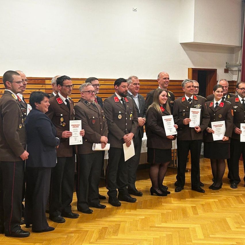 A group of uniformed individuals stand in a hall, holding certificates and posing for a photo. They are in a semi-circle, with a woman in a suit in the middle.