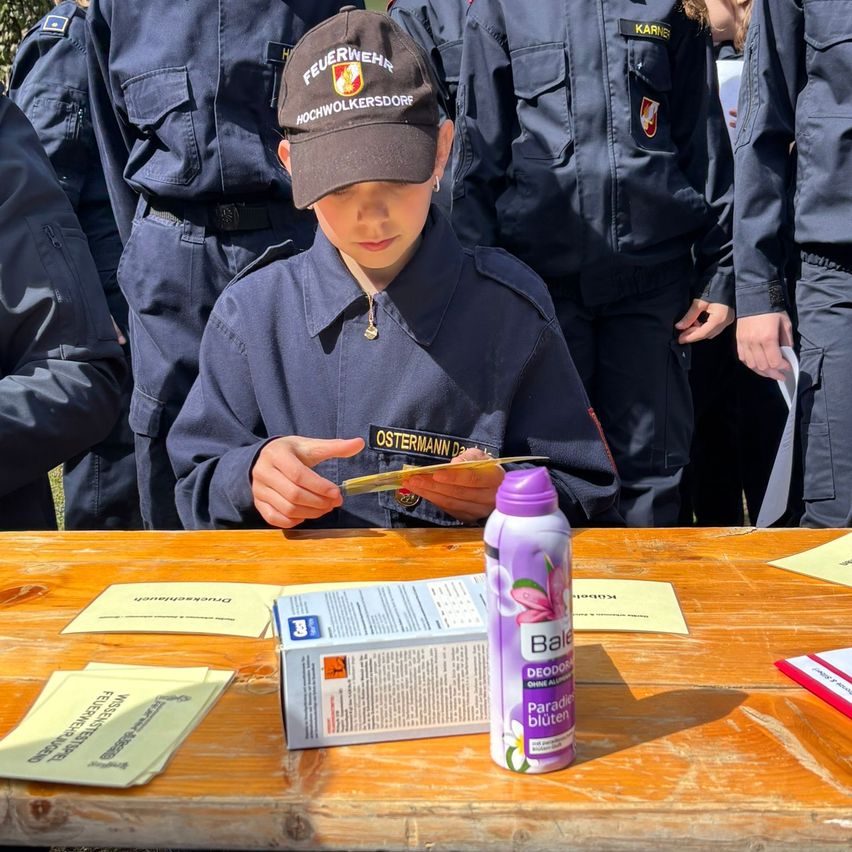 A boy in a uniform sits at a table, holding a yellow slip, with a bottle of 'Paradise' next to a box. Behind him, several people in uniforms stand.