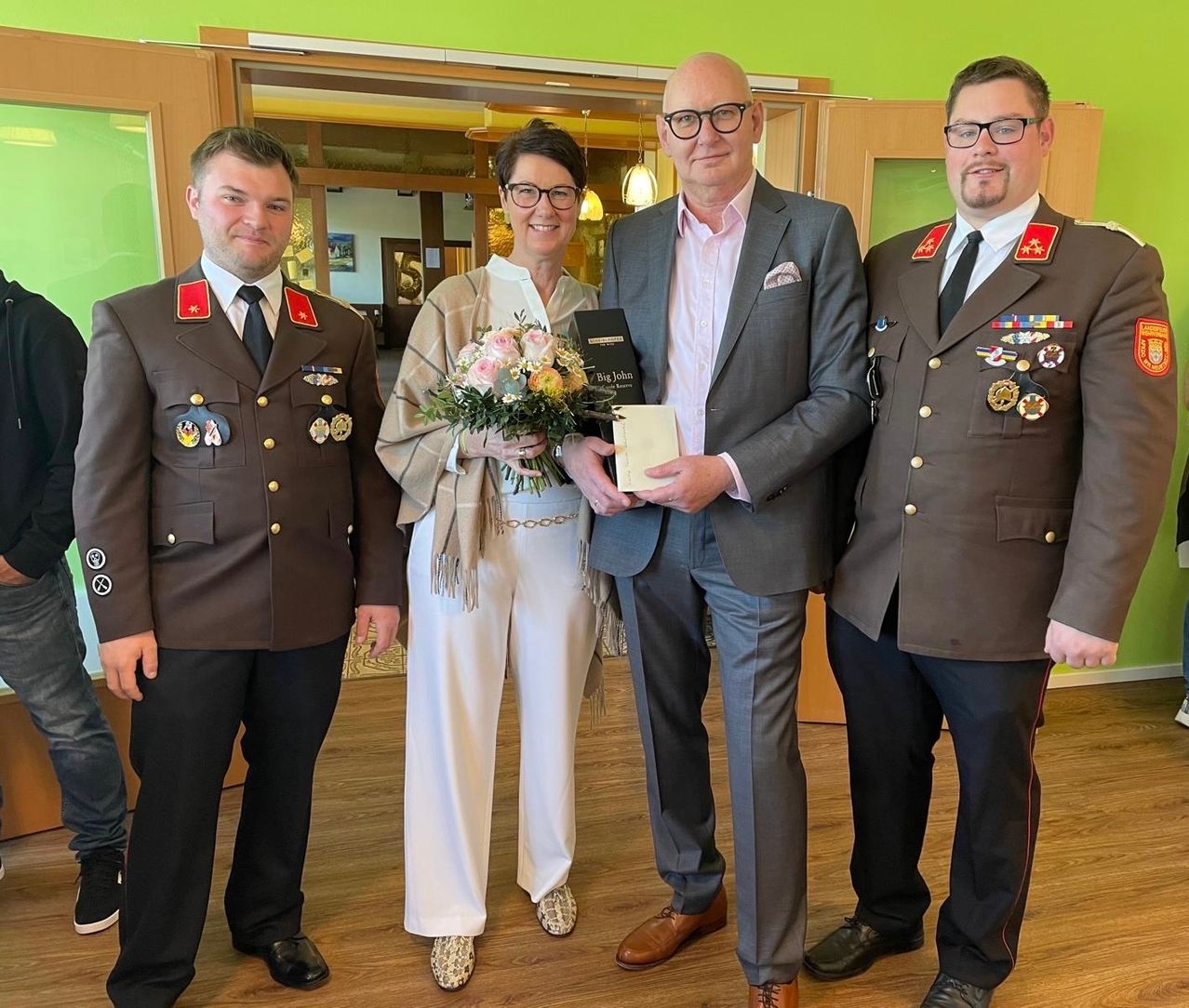 Four people stand close together, holding a bouquet and an award book. They are dressed in formal uniforms.
