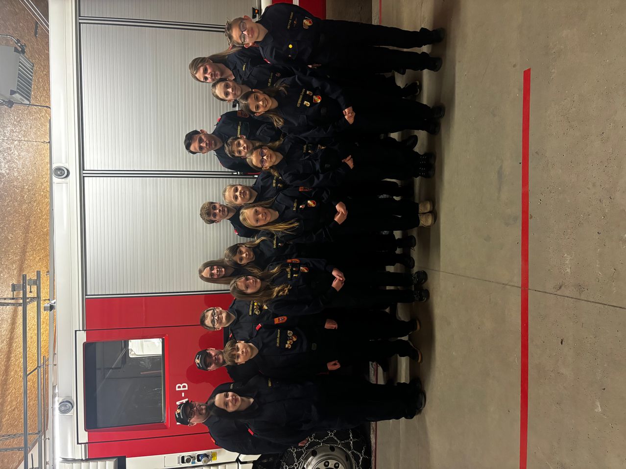 A group of firefighters in uniform stand in front of a red fire truck. They are smiling and posing for a picture.