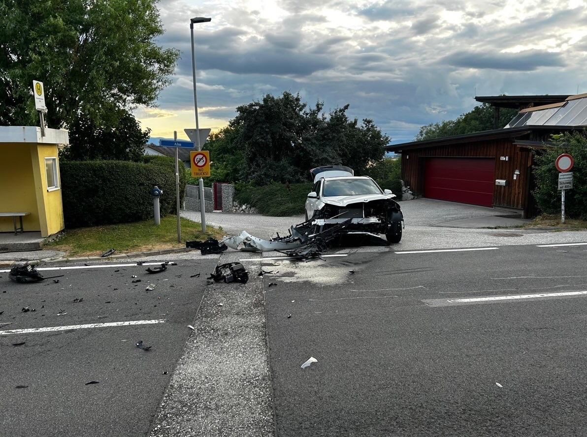 A car is wrecked on a street with debris scattered around, near a street light and a signboard.