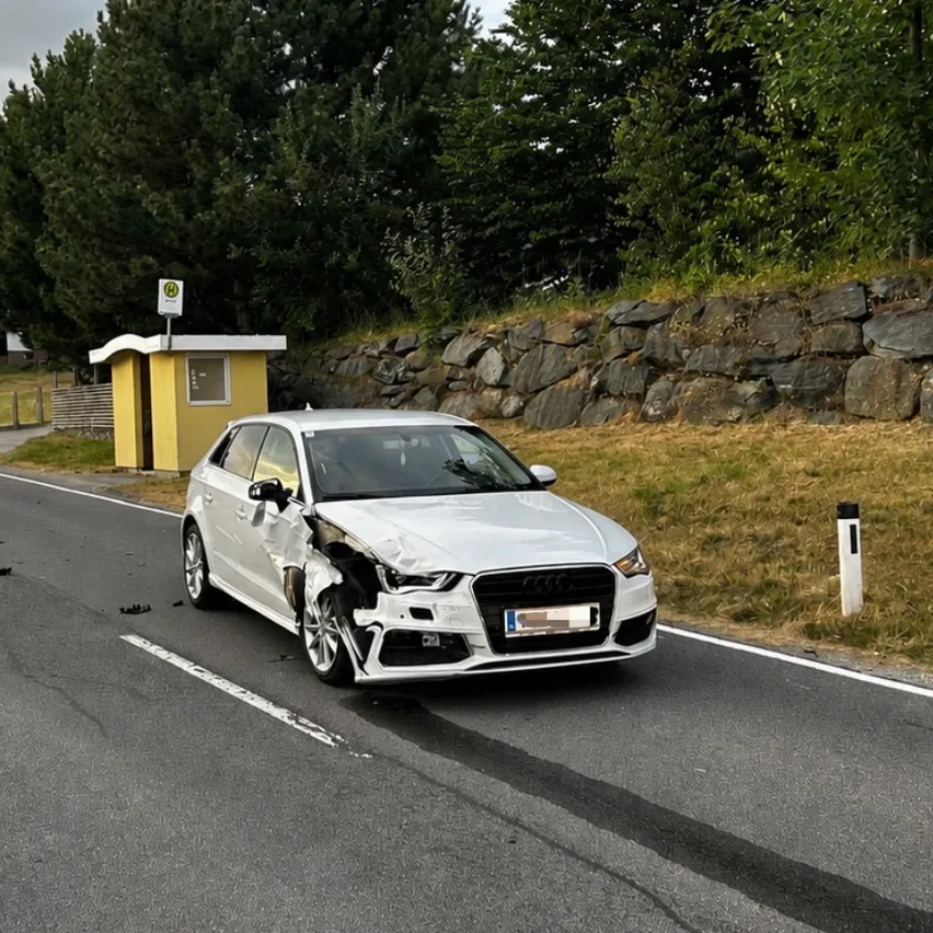 Ein silberner Audi A3 mit Frontschaden steht am Straßenrand. Das Auto hat ein Nummernschild und befindet sich in der Nähe einer Steinmauer.