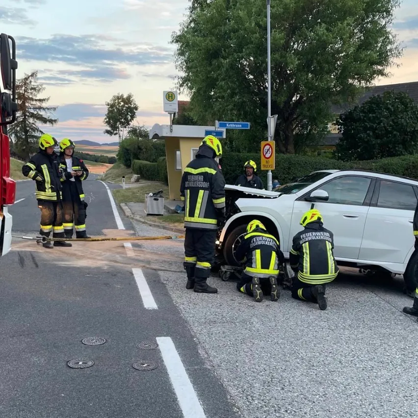 Feuerwehrleute arbeiten an einem beschädigten Auto am Straßenrand, wobei eine Person das Fahrzeug überprüft und andere helfen.