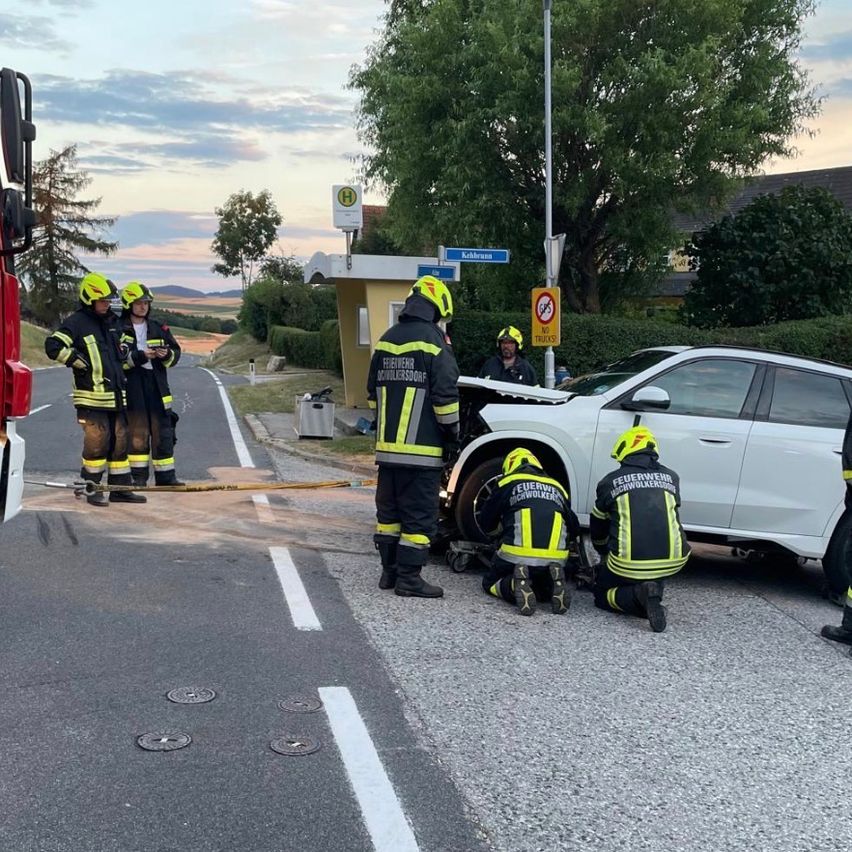 Firefighters are working on a damaged car on the side of the road, with one person checking the vehicle while others assist.
