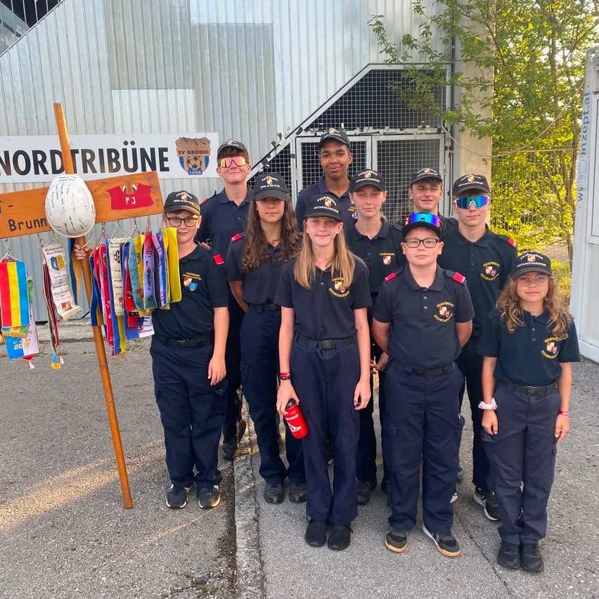 Eine Gruppe junger Menschen in Uniform, möglicherweise Pfadfinder, steht vor einem Gebäude mit einem Banner, auf dem 'Nordtribune' steht. Sie posieren für ein Foto mit Medaillen und einem Helm im Display.