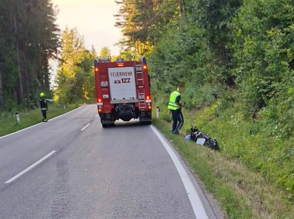 Unfallstelle mit Feuerwehrauto und umgekipptem Motorrad am Straßenrand in Waldnähe
