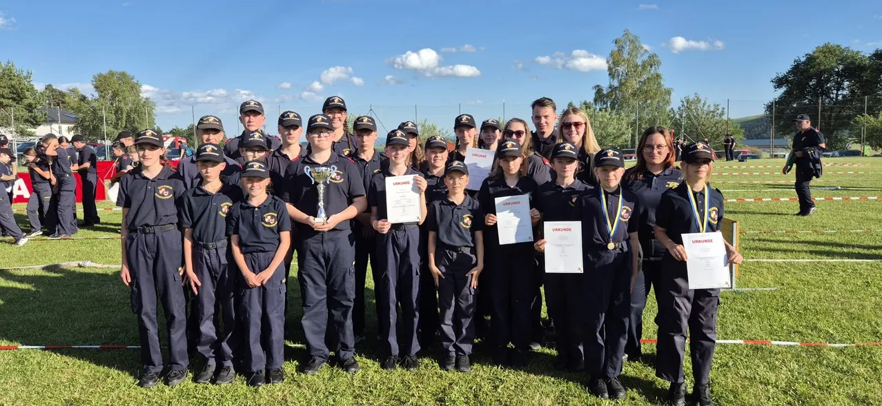 Eine Gruppe junger Leute in Uniform mit Urkunden und einem Pokal posiert für ein Foto auf dem Rasen.