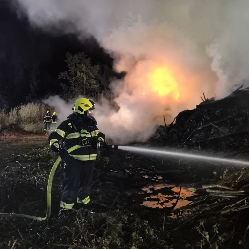 Ein Feuerwehrmann sprüht Wasser aus einem Schlauch, um ein Feuer auf einem Feld bei Nacht zu löschen.