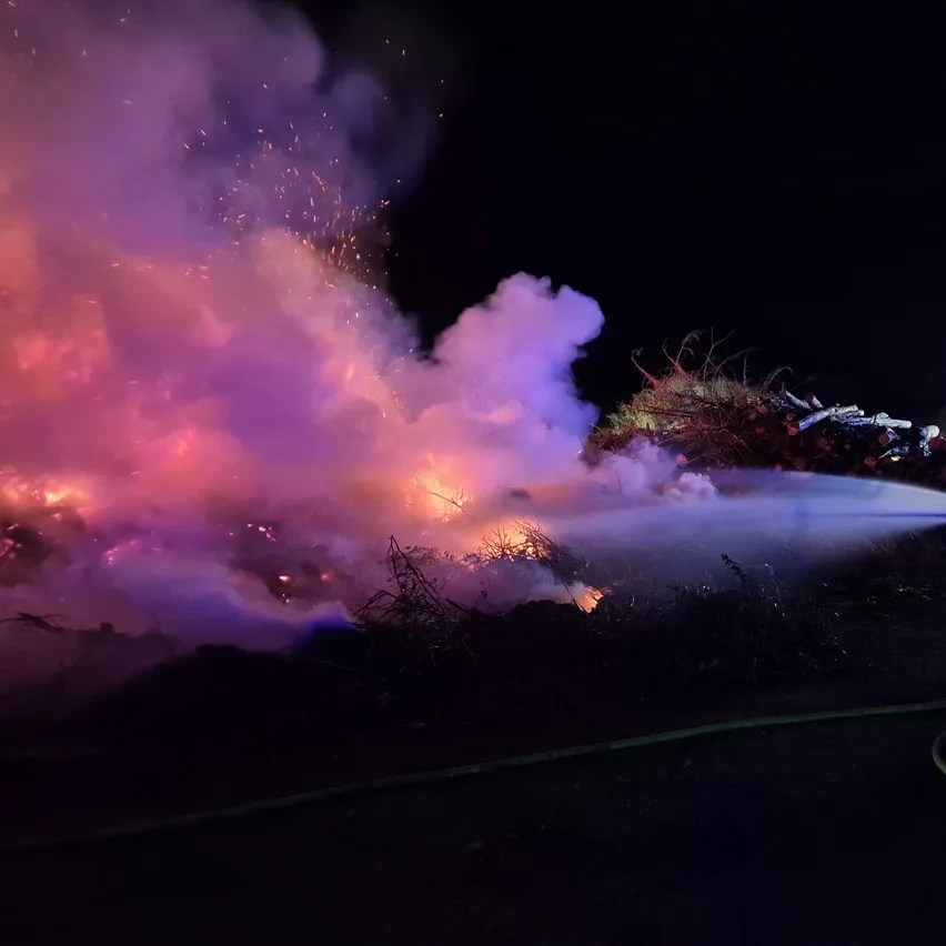 In der Nacht bekämpfen Feuerwehrleute ein großes Feuer, das einen Haufen Schutt erfasst hat. Das Feuer produziert dicken Rauch und Flammen.