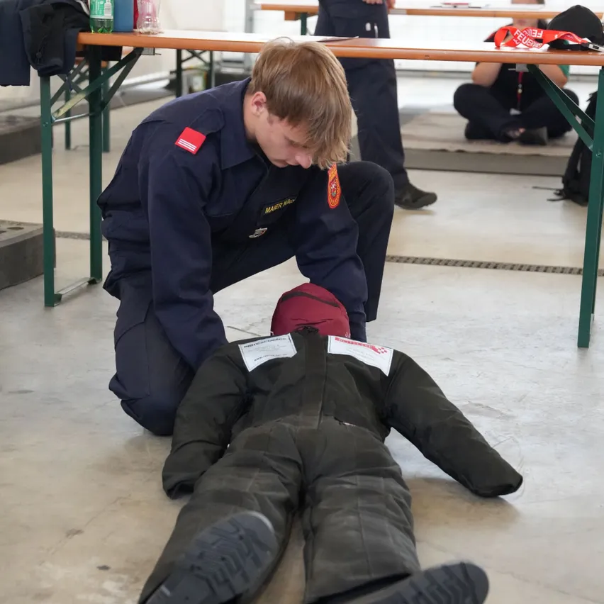 Ein Mann in Uniform kniet und untersucht eine Puppe, die eine schwarze Jacke und Hose trägt.
