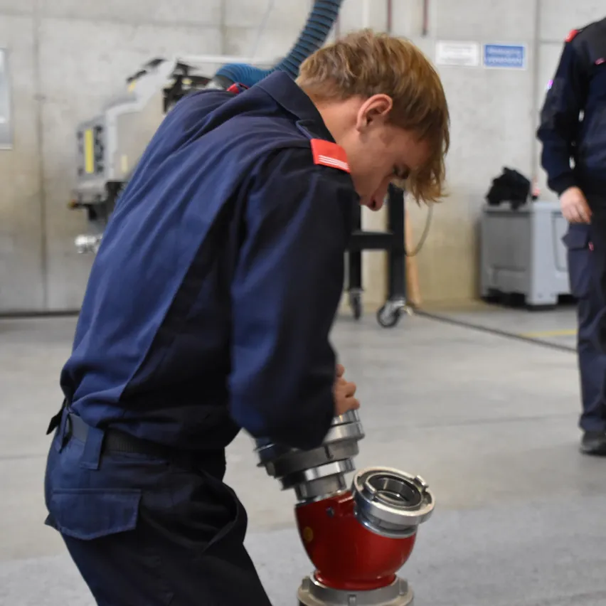 Ein Mann in einer blauen Uniform arbeitet an einer rot-silbernen Maschine in einer Werkstatt.