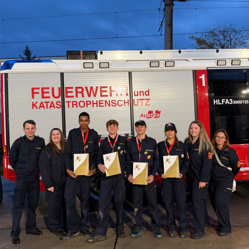 Eine Gruppe von Feuerwehrleuten in Uniform steht vor einem Feuerwehrauto.